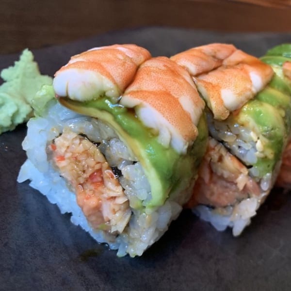 Sushi Mike's shrimp and avocado sushi rolls with wasabi on a dark plate.