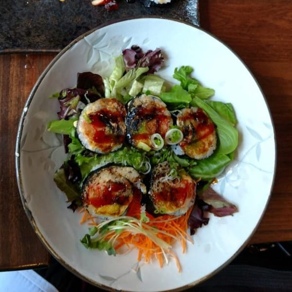 Sushi Mike's fried sushi rolls with sauce, green onions, and shredded carrots on a bed of lettuce.