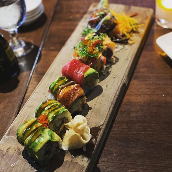 A wooden board holds a variety of colorful sushi rolls, including avocado, tuna, and eel.