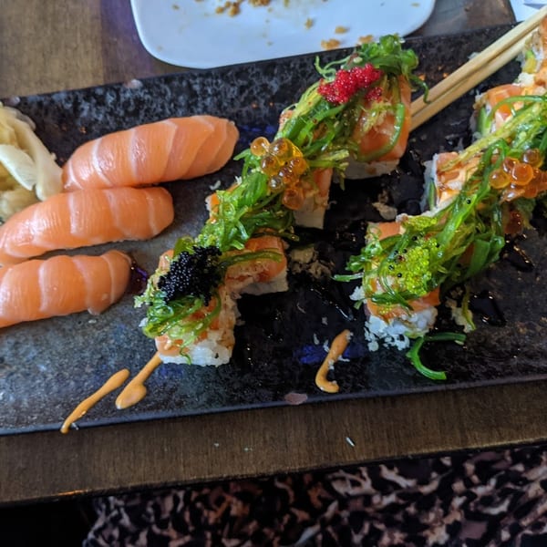 A black platter of Sushi Mike's salmon nigiri and sushi rolls topped with seaweed salad and roe.