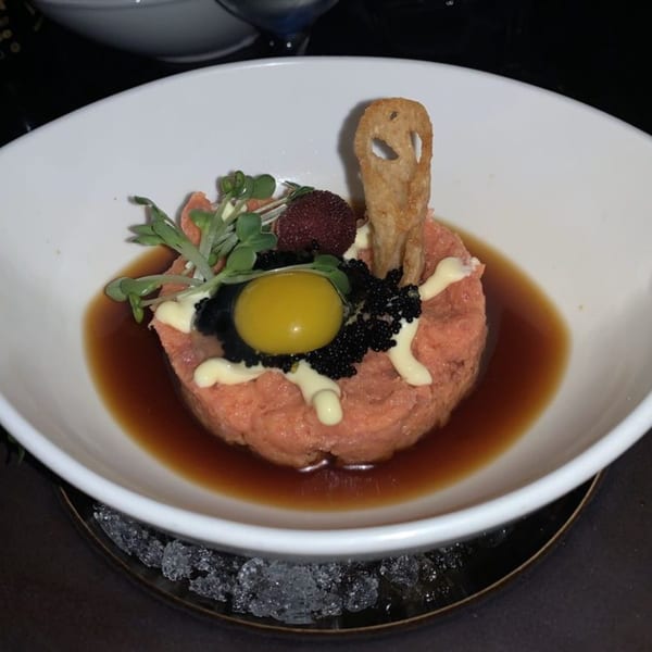 Sushi Mike's salmon tartare with quail egg, caviar, and microgreens in a white bowl.