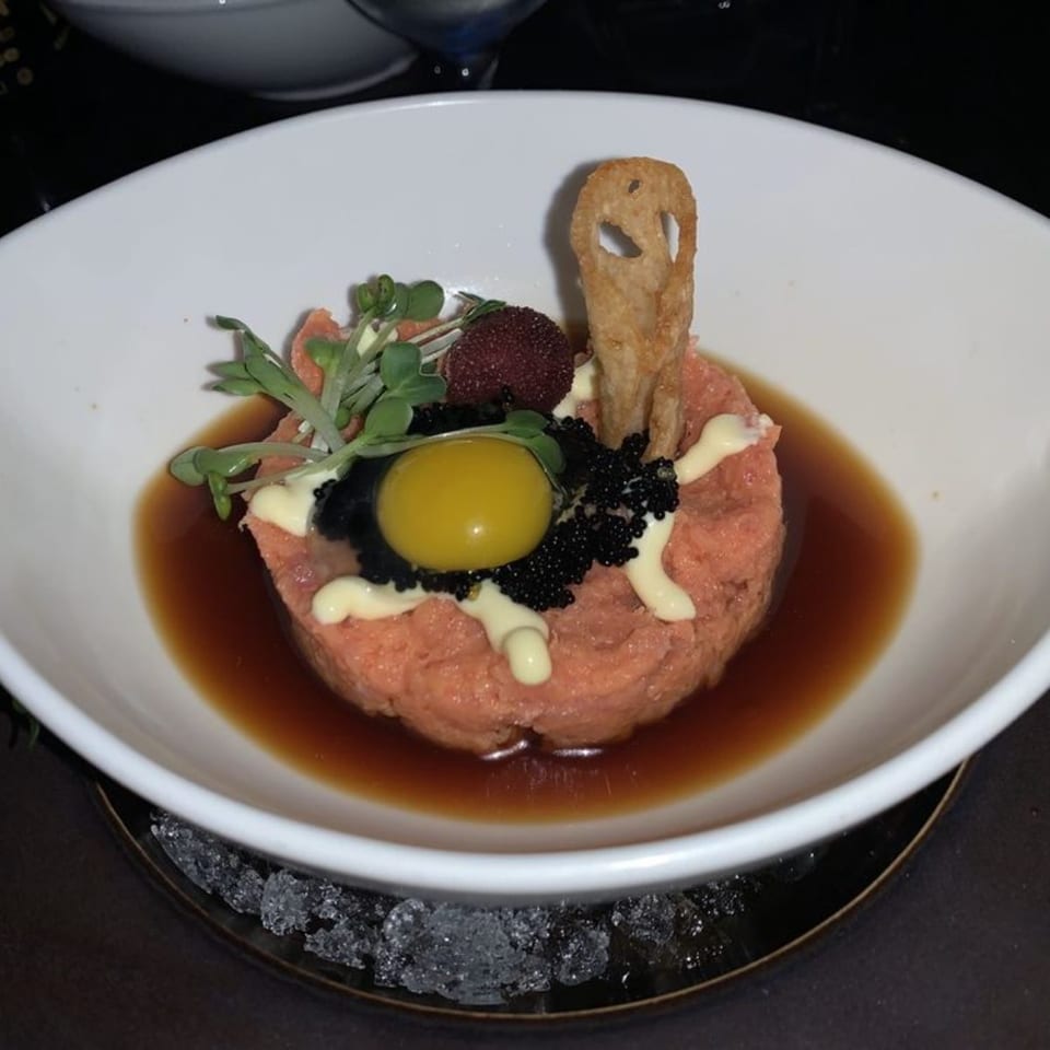 Sushi Mike's salmon tartare with quail egg, caviar, and microgreens in a white bowl.